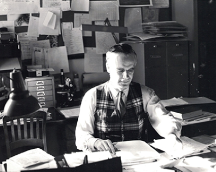 Dr. Murray sitting at a desk, sorting papers. Photo in black and white.